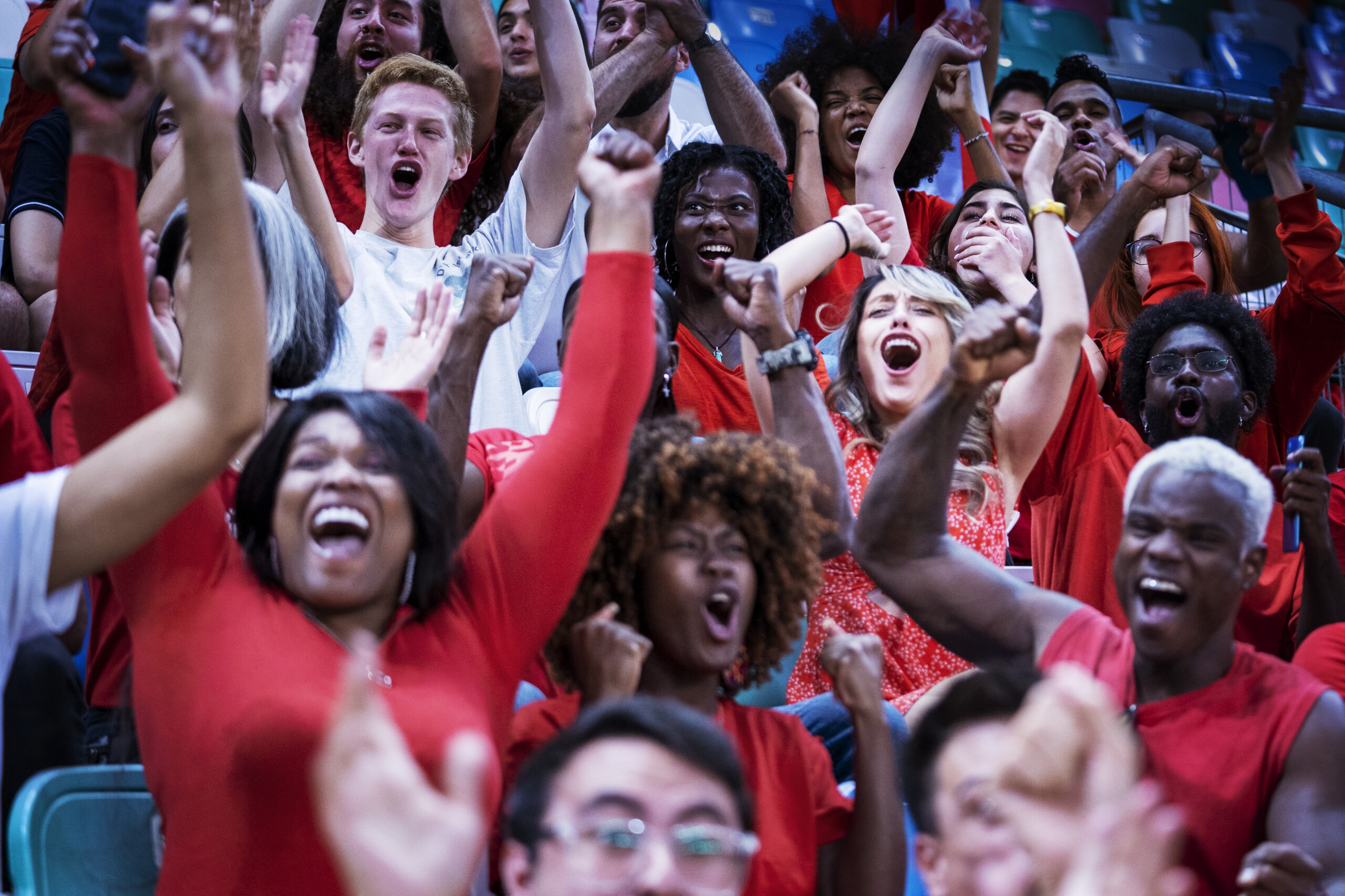 Ecstatic crowd sitting in the bleachers of a crowded sports stadium raise their hands up and cheer loudly during a professional soccer match as their favorite home football league takes the lead