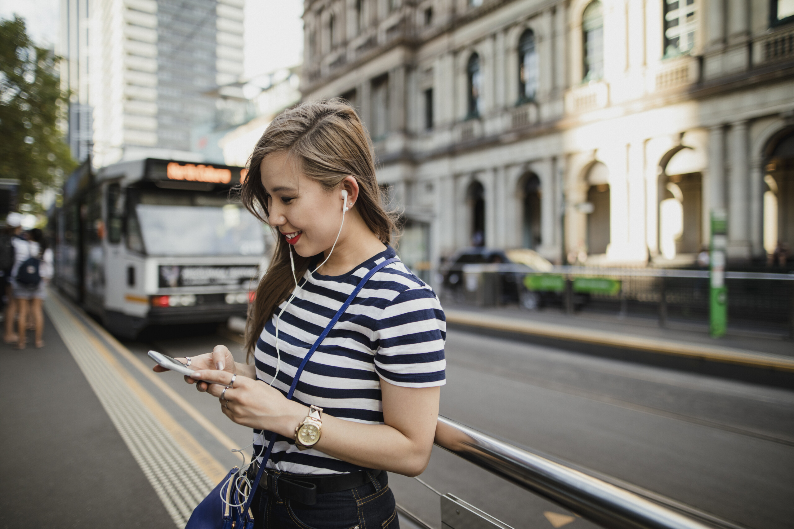 Young Asian woman using a smartphone as she waits for a tram in Melbourne CBD.