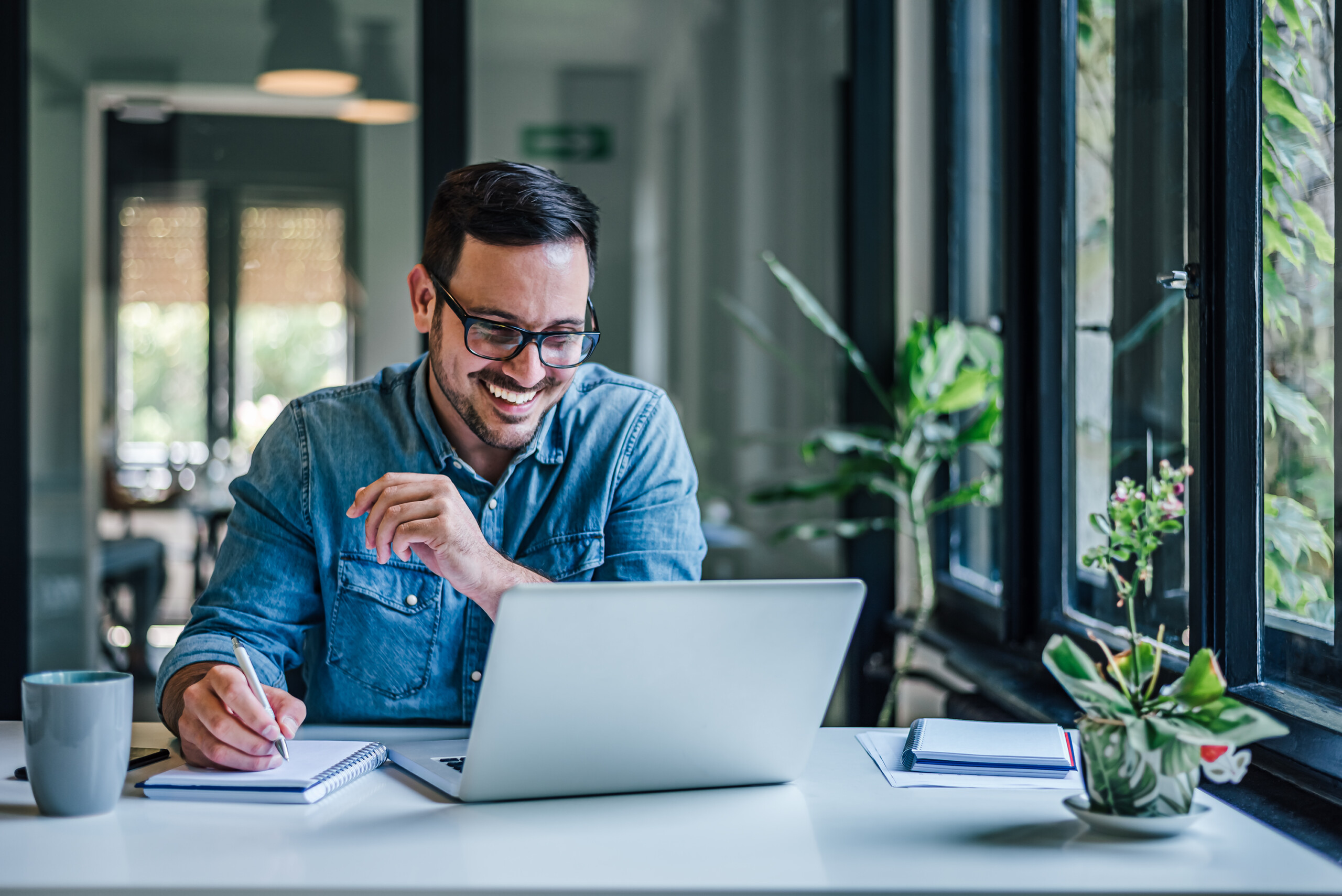 Cheerful adult man with glasses, taking notes on the conference call.