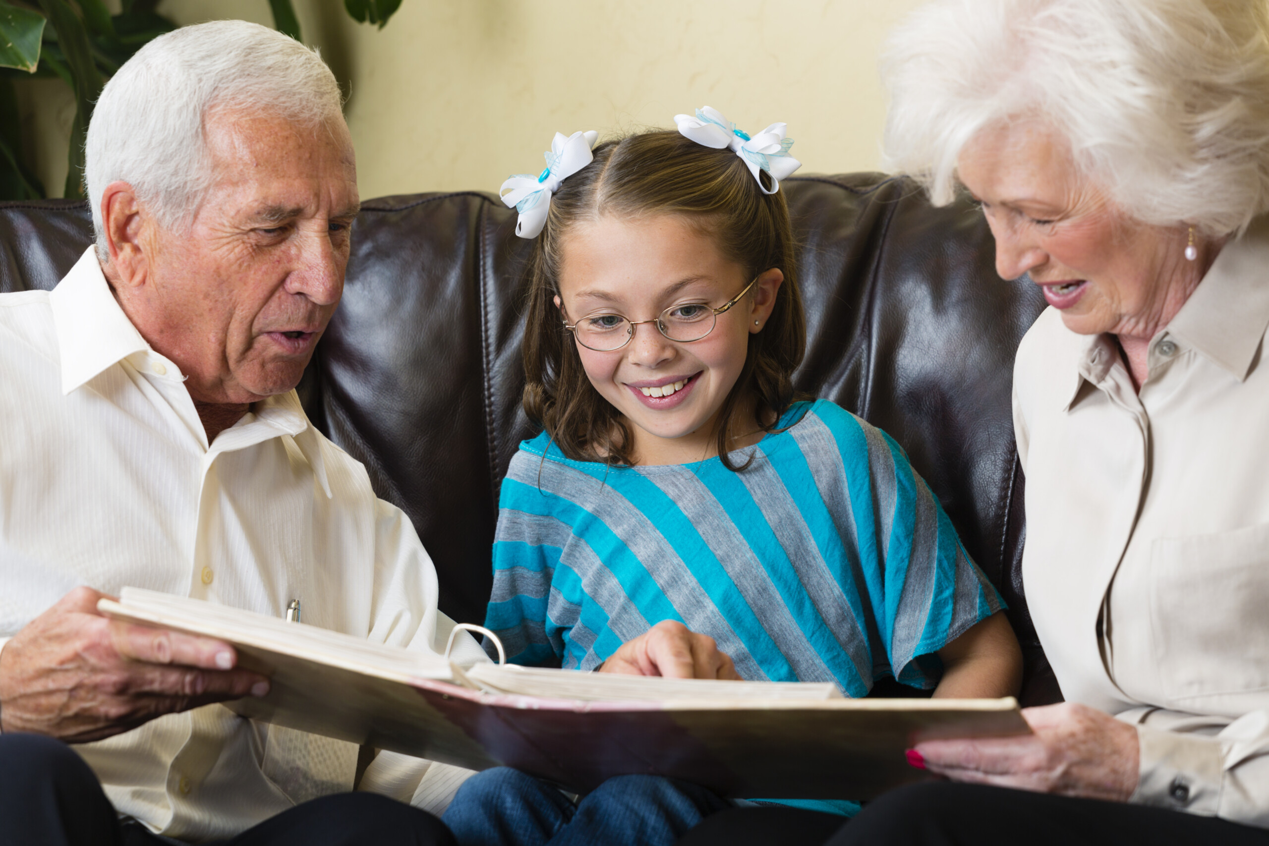 A senior citizen couple sitting on a couch with a little girl, looking at a photo album.