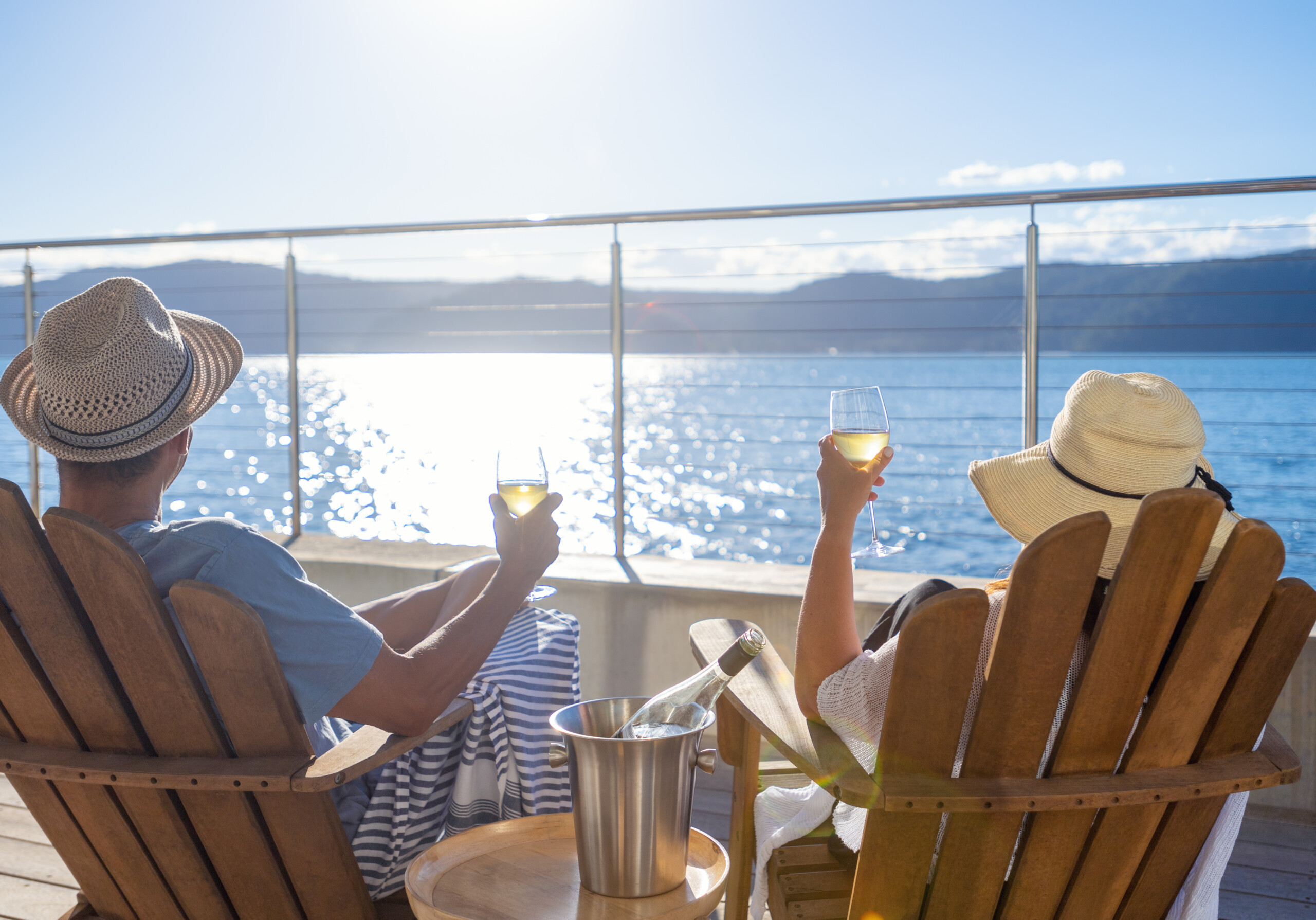 Couple relaxing and drinking wine on deck chairs in an over water bungalow. They are holding the wine glasses