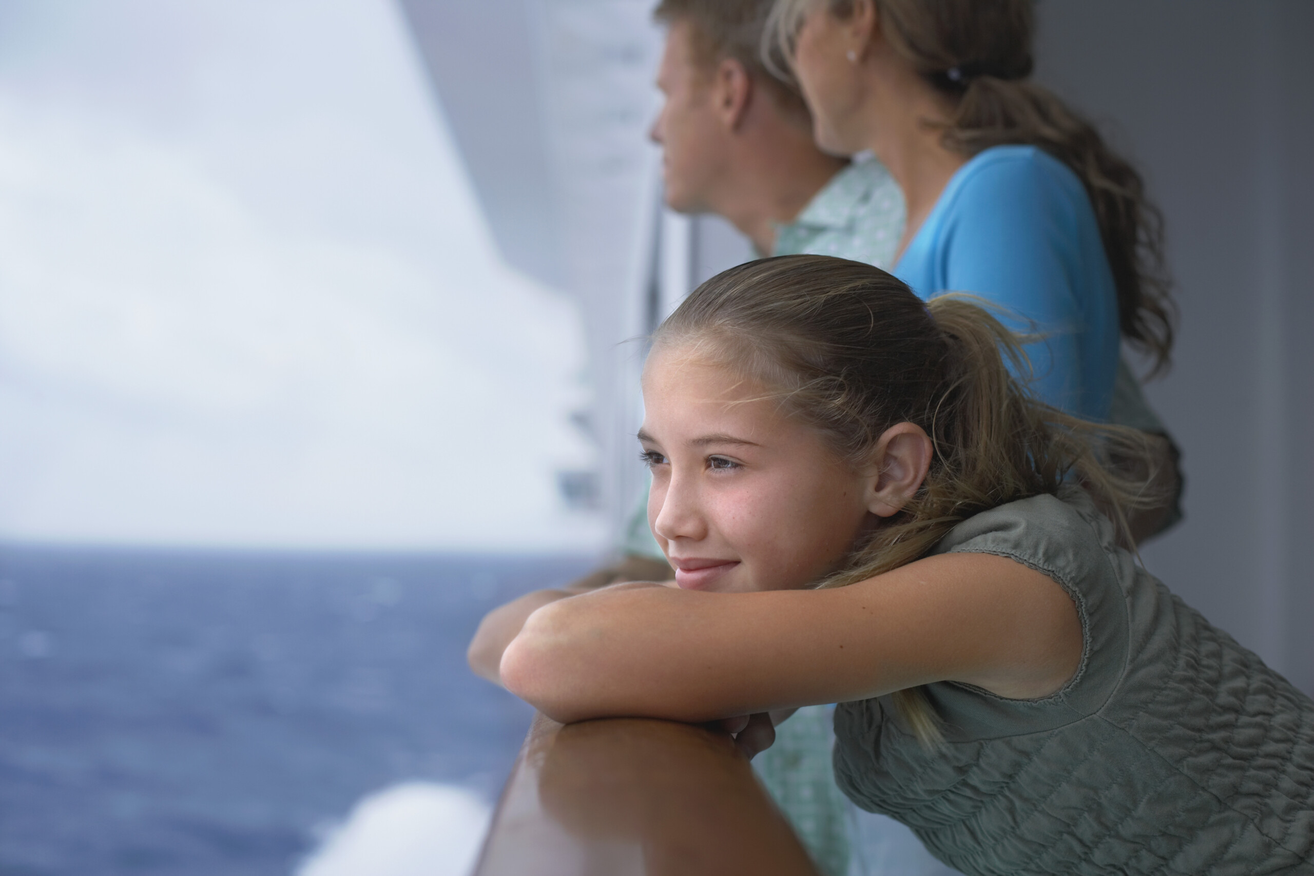 Girl (10-12) leaning on rail of cruise ship, parents in background