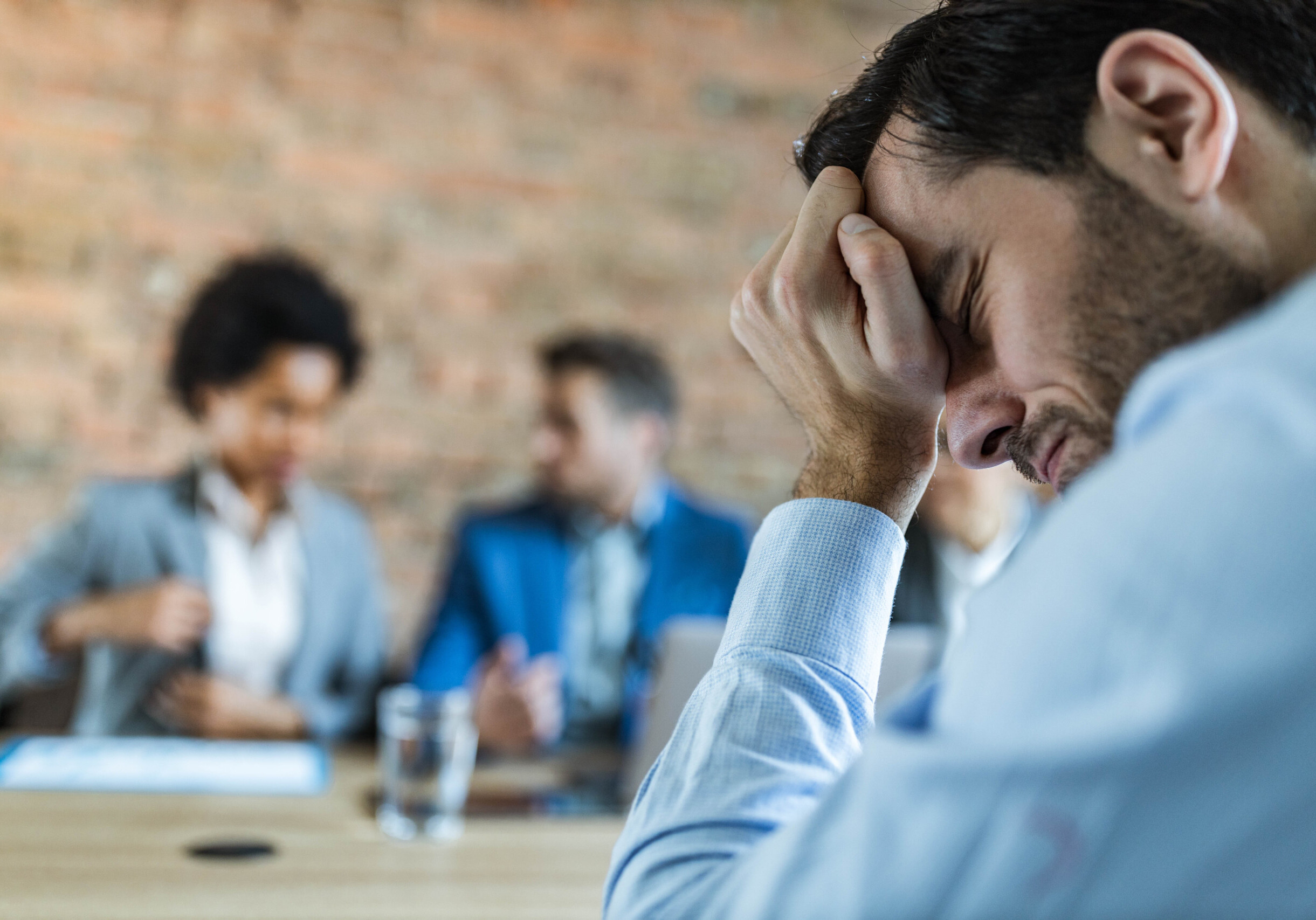 Young male candidate feeling pain in his head while being on a job interview in the office.