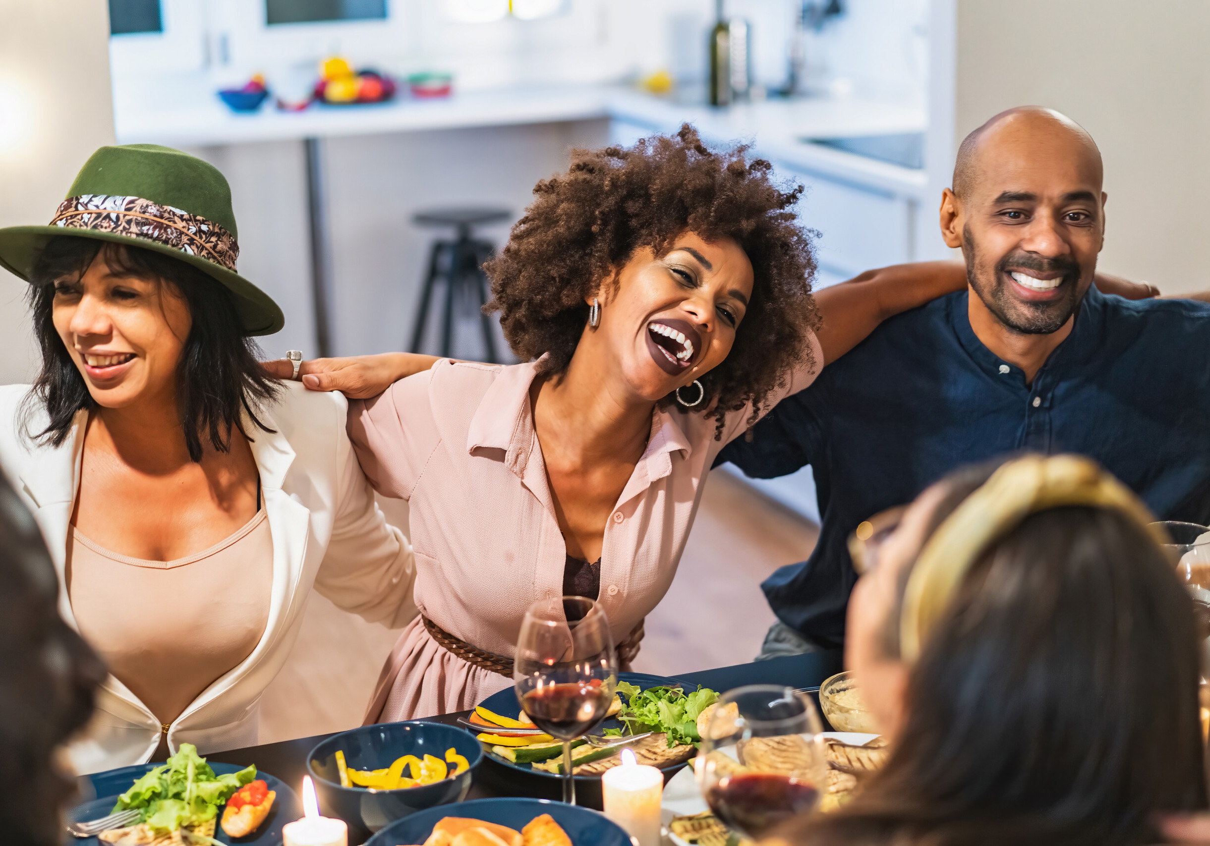 An interracial party of adult friends gathered for dinner is having fun. Forty-year-olds hugging arms on shoulders and laughing together happily, hugging and singing.