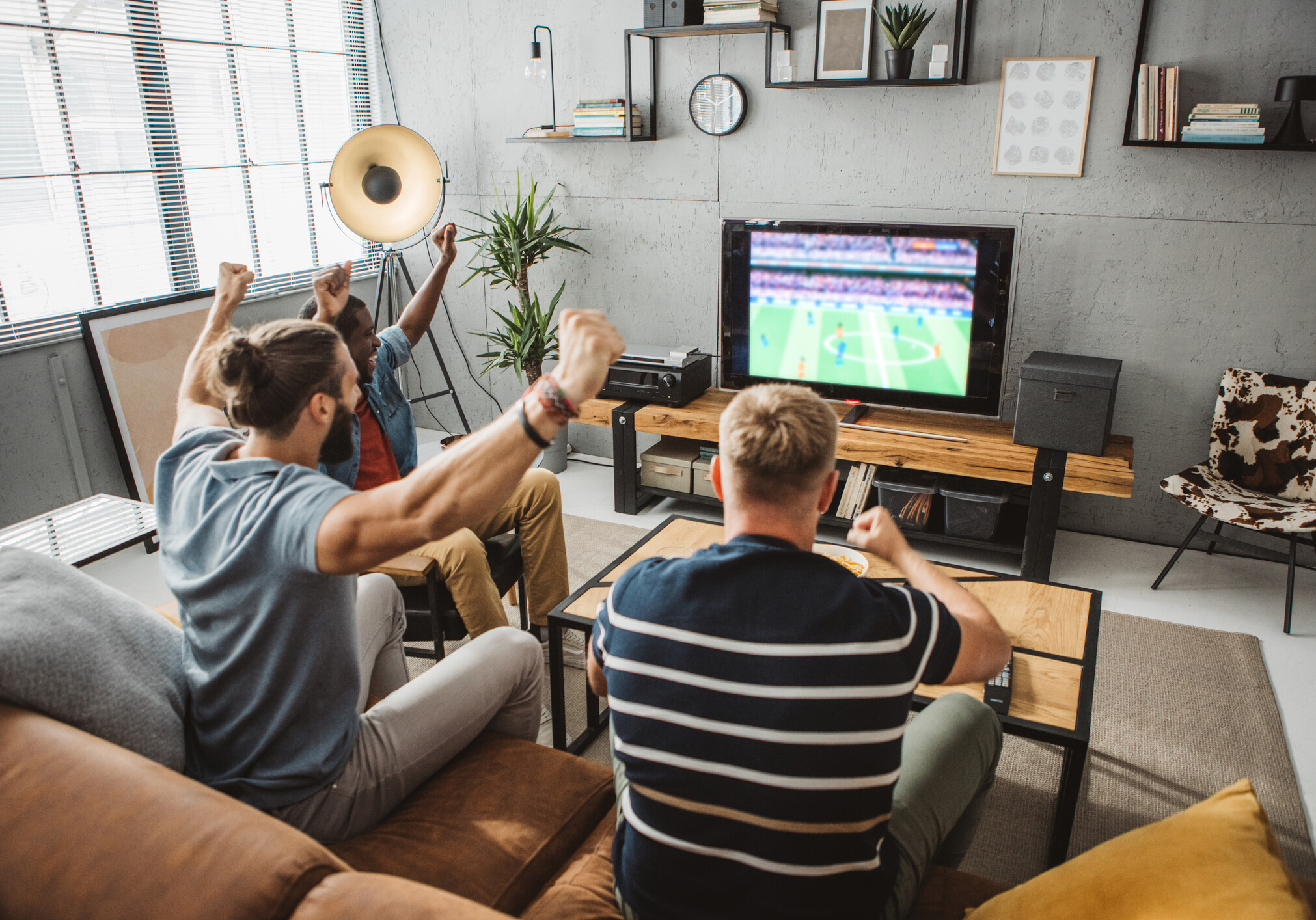 Diverse group of men watching soccer match at home and cheering for favorite team.