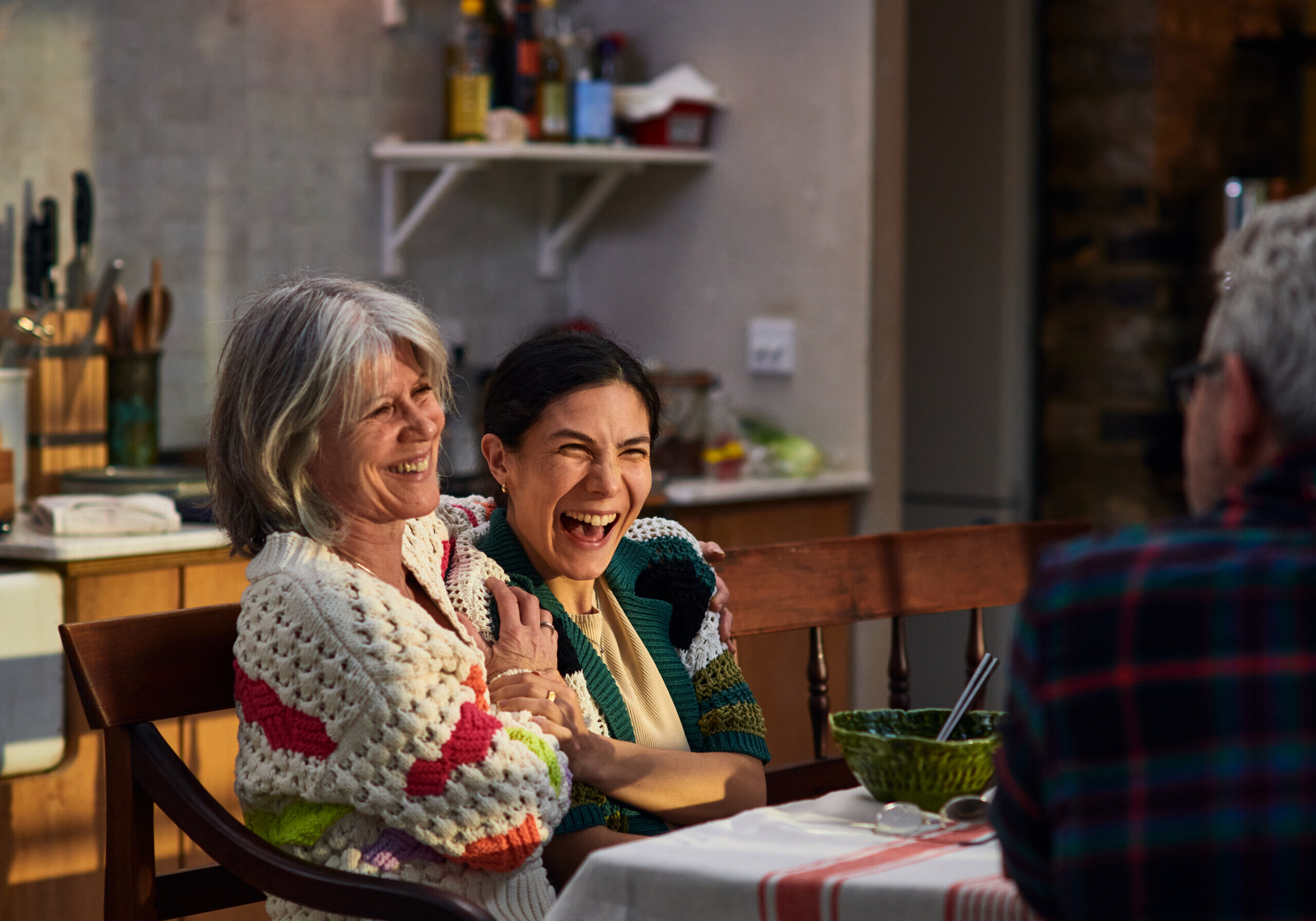 Woman in her 30's on home visit to parents sitting at table enjoying meal with her parents, smiling and laughing, enjoyment, togetherness, bonding